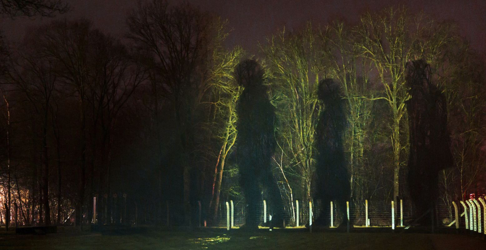 Op bomen en muren doemen schaduwen op van mannen, vrouwen en kinderen. Foto: Anna van Kooij