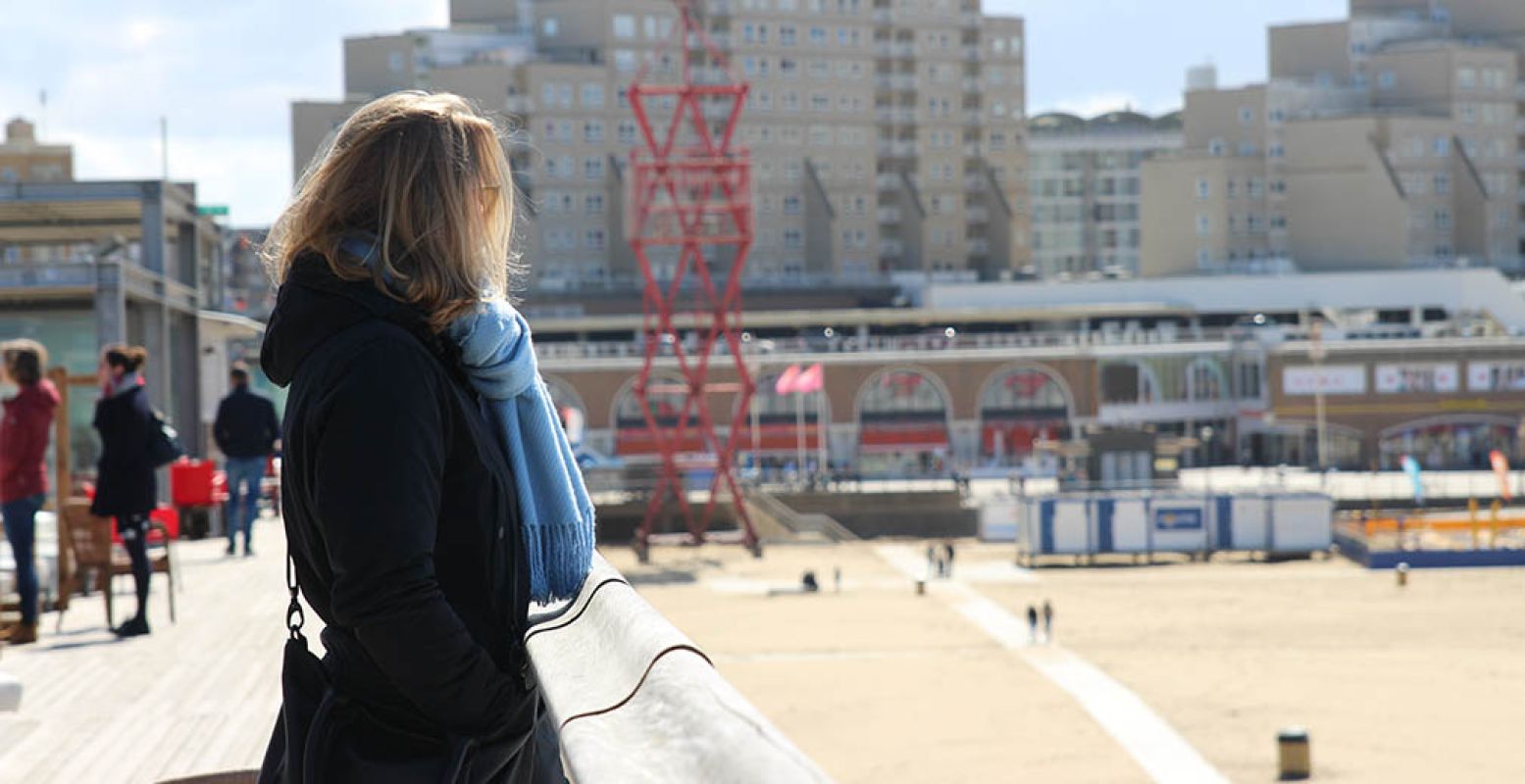 Vrouw kijkt over het strand uit vanaf De Pier. Foto: Redactie DagjeWeg.NL.