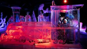 Mensen kijken door het raam van een grote en roodblauw verlichte locomotief van ijs op het IJsbeelden Festival Foto: Foto: IJsbeelden Festival
