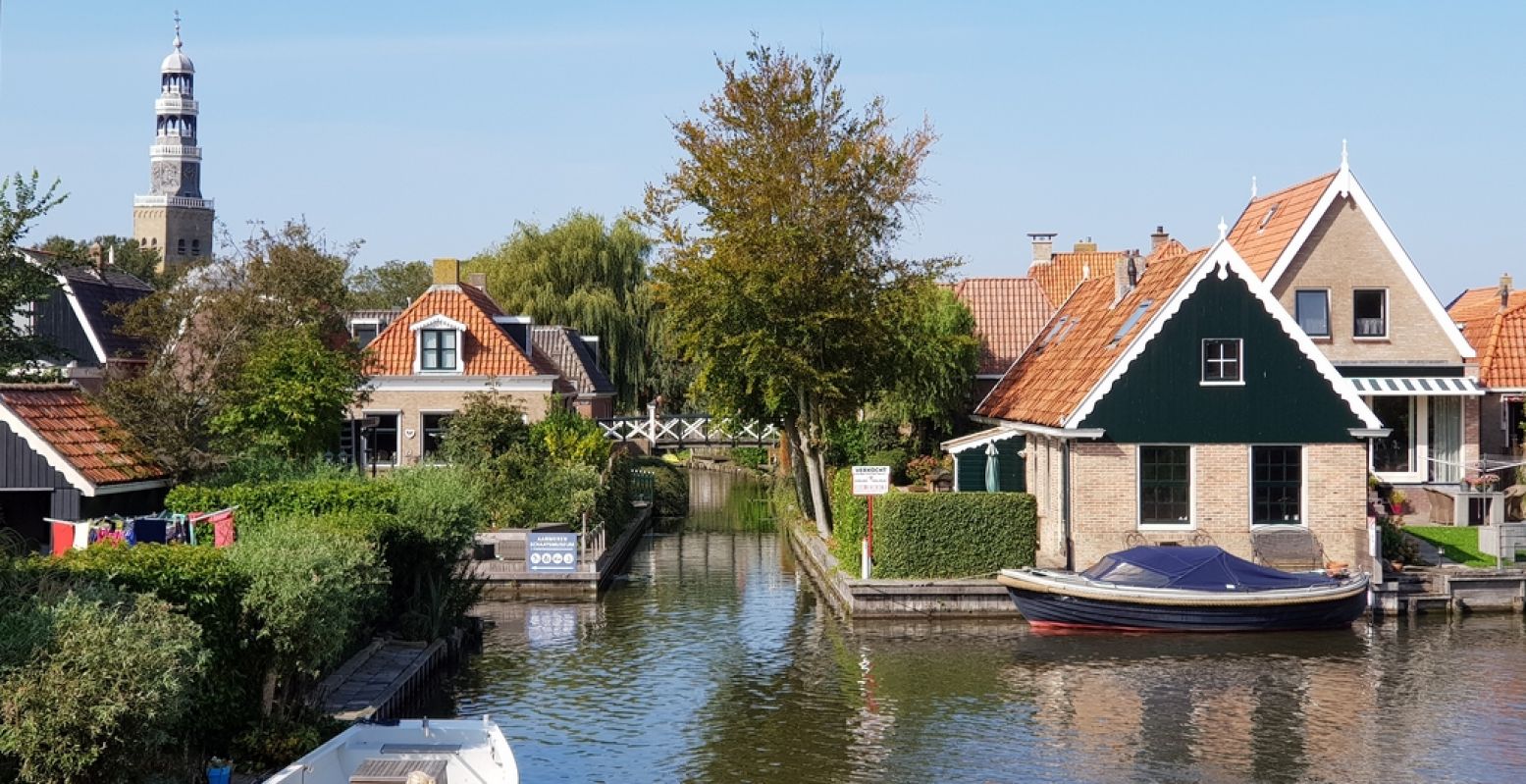 Een doorkijkje vanaf een van de voetgangersbruggetjes in Hindeloopen. Op de achtergrond de typische toren van de Grote Kerk, die zo scheef staat als de toren van Pisa. Foto: DagjeWeg.NL © Tonny van Oosten