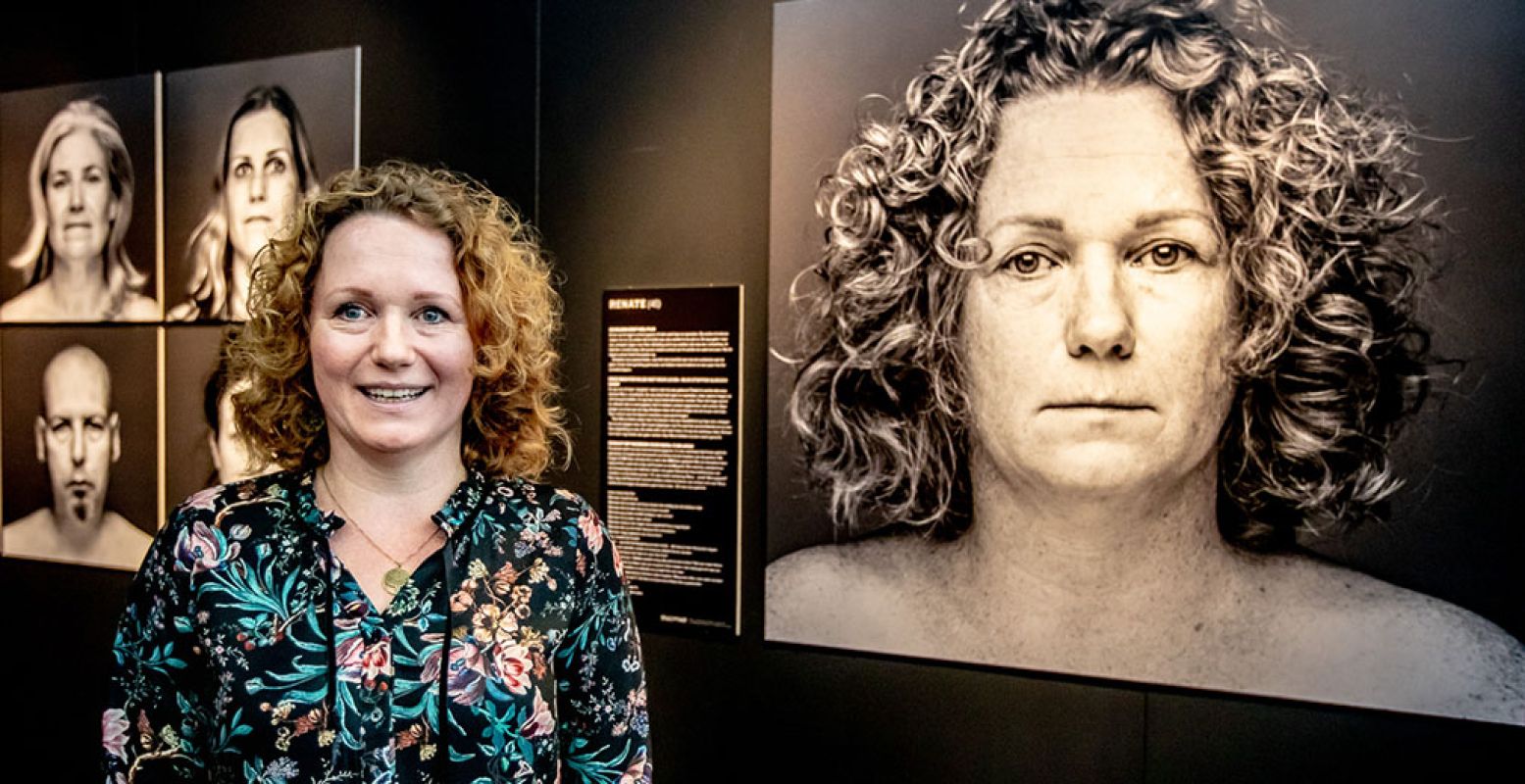 Renate bij haar portret, gemaakt door Susan Leurs, tijdens de opening van de tentoonstelling Pesten. Naast het portret haar verhaal. Ook haar dochter is te zien in de tentoonstelling. Foto: Jean-Pierre Geusens in Centre Céramique