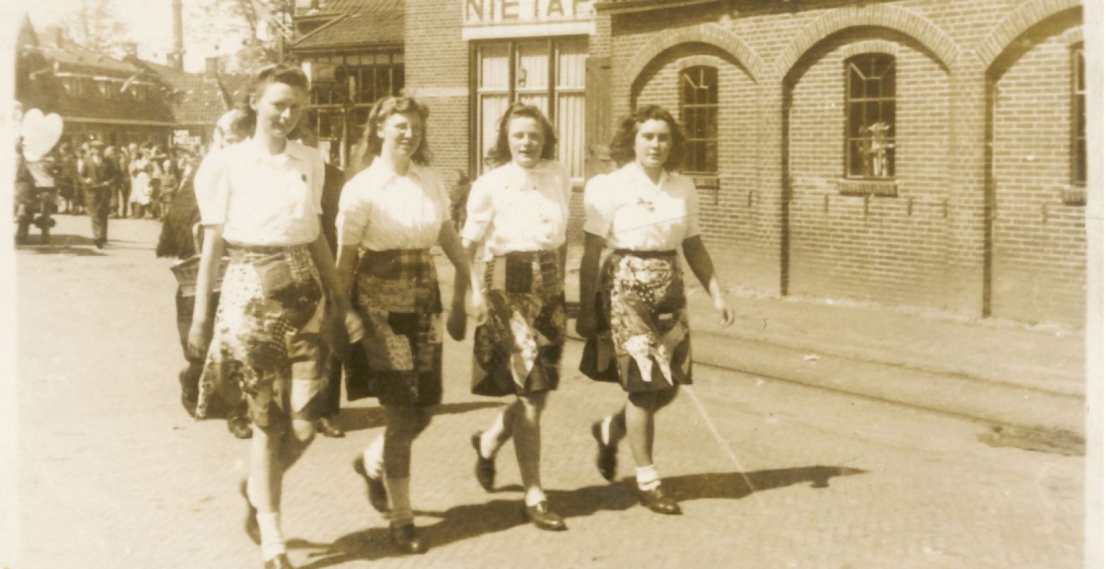 Vier meisjes (vlnr: Roelie v/d Velde, Lina Harms, Stien Bosman en lepie Buitenkamp) in hun Bevrijdingsrok, meelopend in de optocht ter gelegenheid van Koninginnedag 1946 in Leek-Nietap. Foto: Groninger Archieven.
