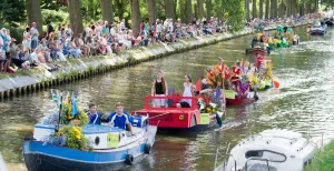 Varend Corso: bungelende benen langs de waterkant Door kinderen versierde bootjes: Kindercorso. Foto: Varend Corso Westland