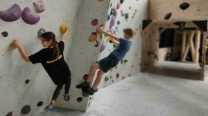 Twee kinderen hangen aan een boulder klimwand bij Be Boulder en kijken hoe ze het beste verder kunnen.