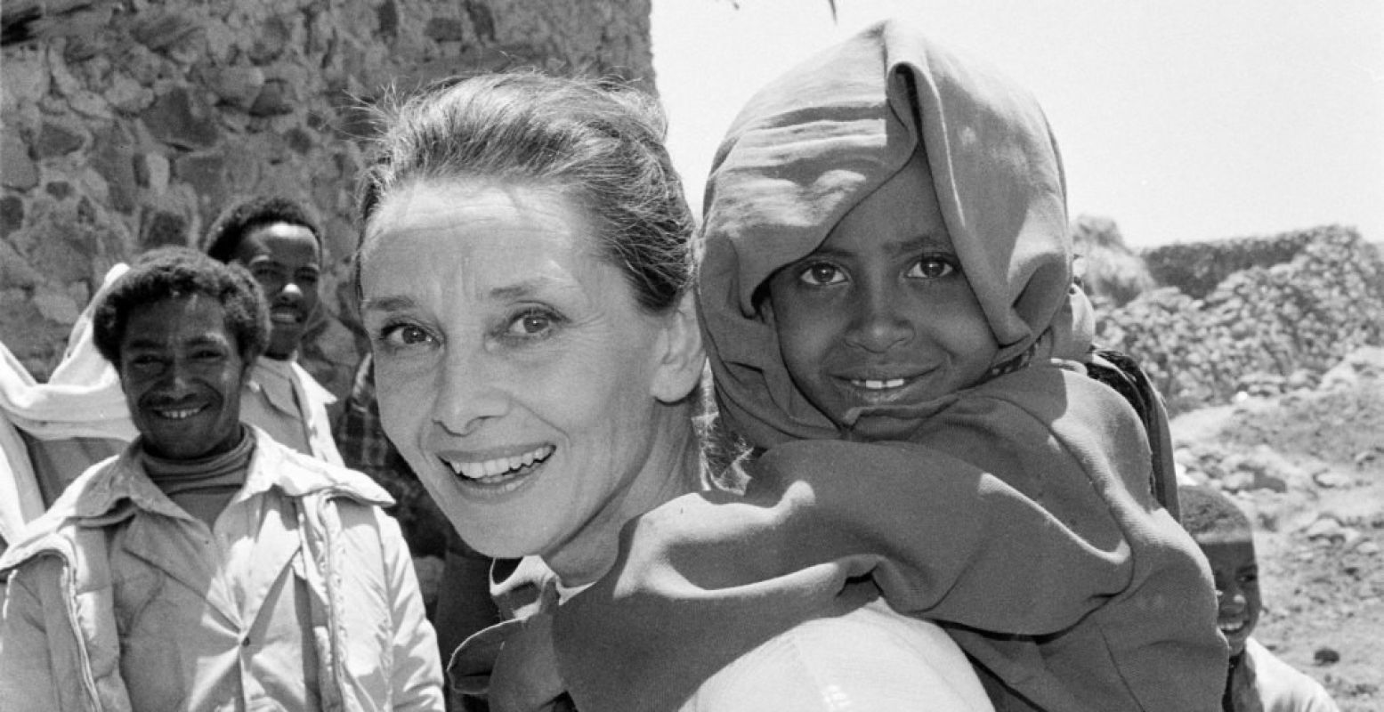 1988 Ethiopië UNICEF Goodwill Ambassador Audrey Hepburn smiles as she carries a child on her back, in the northern town of Mehal Meda in Shoa Province. Ms. Hepburn was visiting a food distribution centre in the town. Foto: John Isaac, © UNICEF/UN