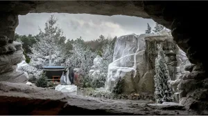 Door een grot zie je een besneeuwde wintertuin met rotsen, dennebomen en pinguïns.