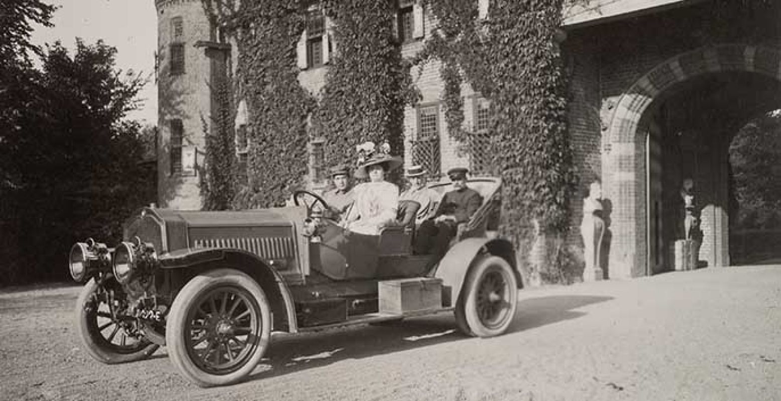 Barones Hélène, de eerste Franse vrouw met een rijbewijs, aan het stuur met chauffeur op achterbank, ca 1906, op oprijlaan voor Châtelet. Foto: Kasteel de Haar